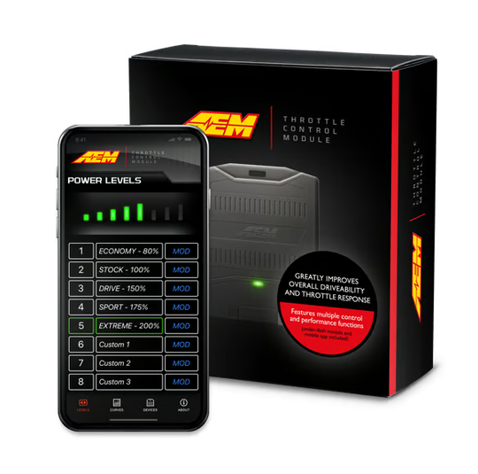A black AEM Throttle Control Module shown in front of its retail box, with a smartphone displaying the AEM app power-level interface. The box is black with orange and red branding and text, and the phone screen is black with green and white interface elements.