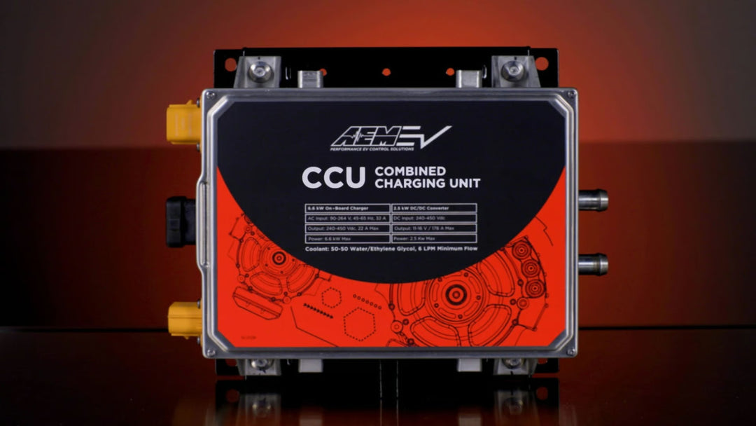 An AEMV CCU Combined Charging Unit with a black and orange front faceplate, set against a dark studio background with a warm orange glow.