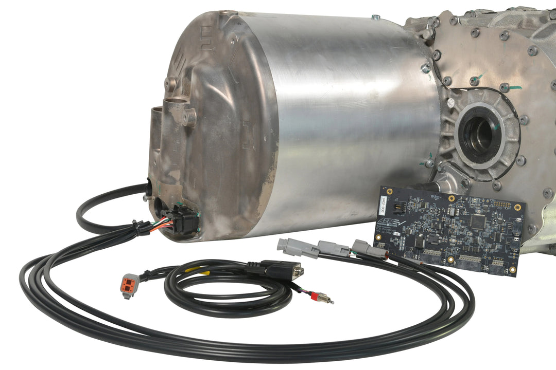 A large metallic industrial motor or transmission component shown on a white background, with attached black cables and a small circuit board placed in front.