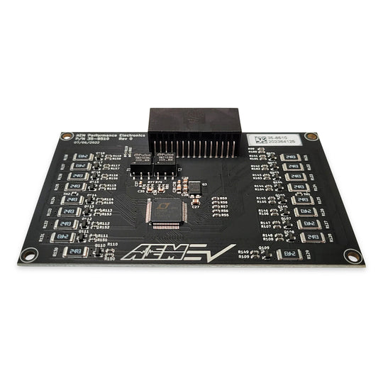 A black automotive electronic control module board with various integrated circuit chips, resistors, and a central black connector block, photographed on a solid white background.